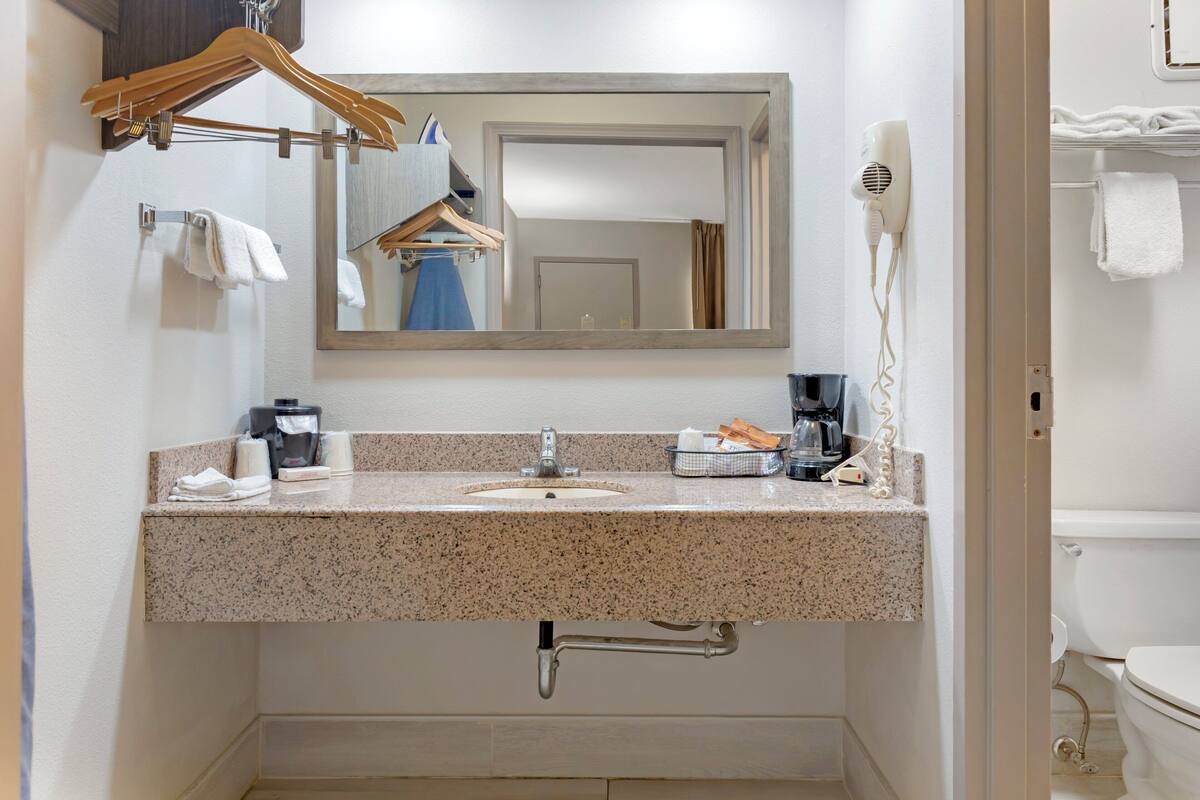 A bathroom with a granite countertop sink, a mirror, a hairdryer, and a towel rack.