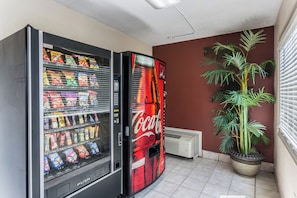A vending machine with a Coca-Cola logo, a potted plant, and a window with blinds. - Red Roof Inn Bowling Green (Bowling Green)