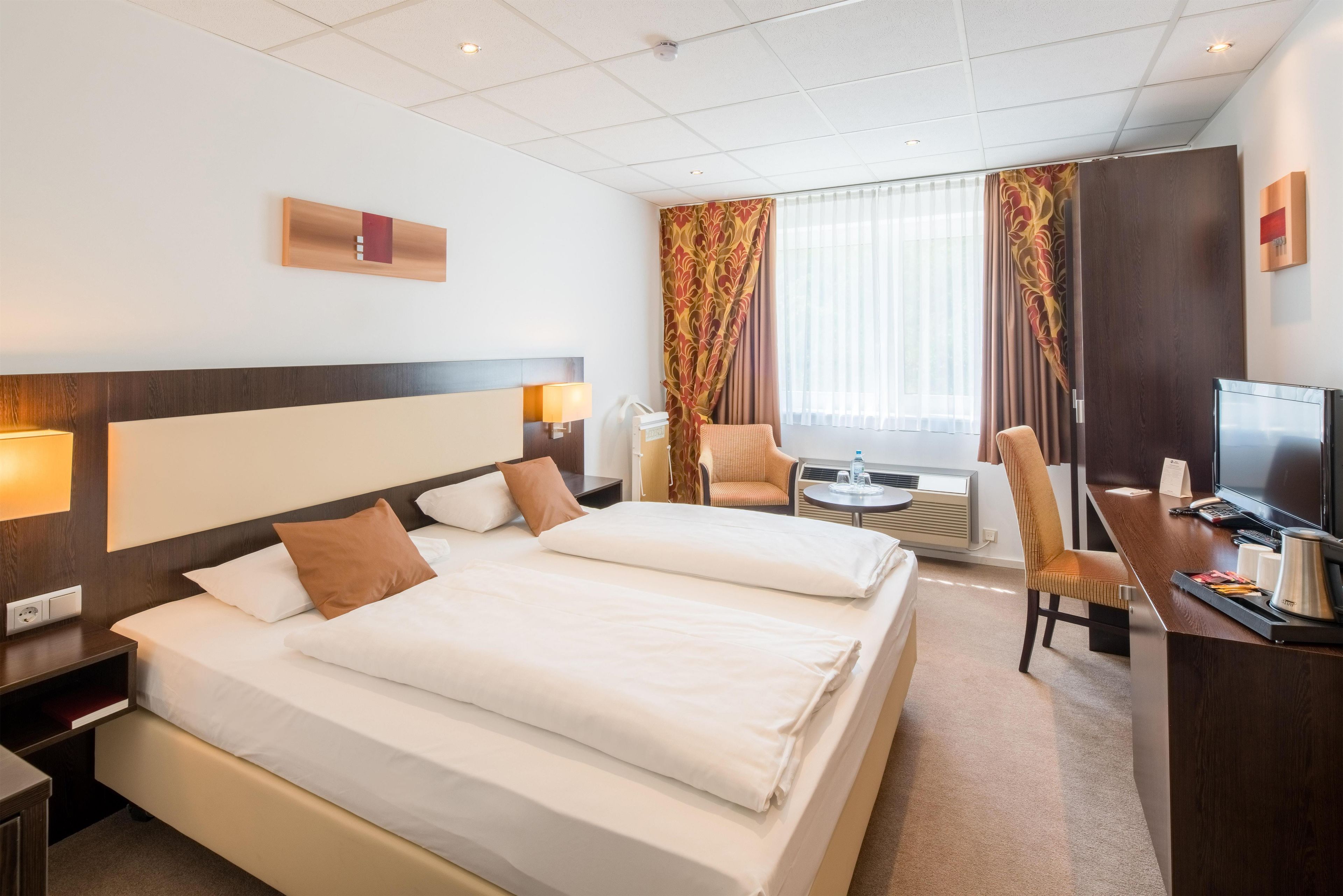 A hotel room with two beds, a desk with a television, and a chair.