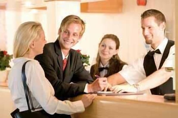 A reception area with a reception desk, a guest seated, and a staff member standing. - Best Western Hotel Jena (Jena)