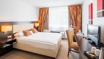 Una habitación de hotel con cama, lámparas de noche, escritorio con televisor, una silla y cafetera.