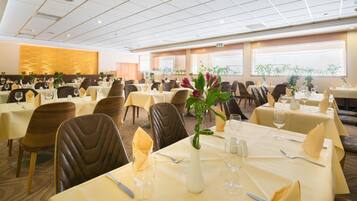 A spacious dining area with multiple tables set for guests, featuring a modern ceiling design and large windows allowing natural light.