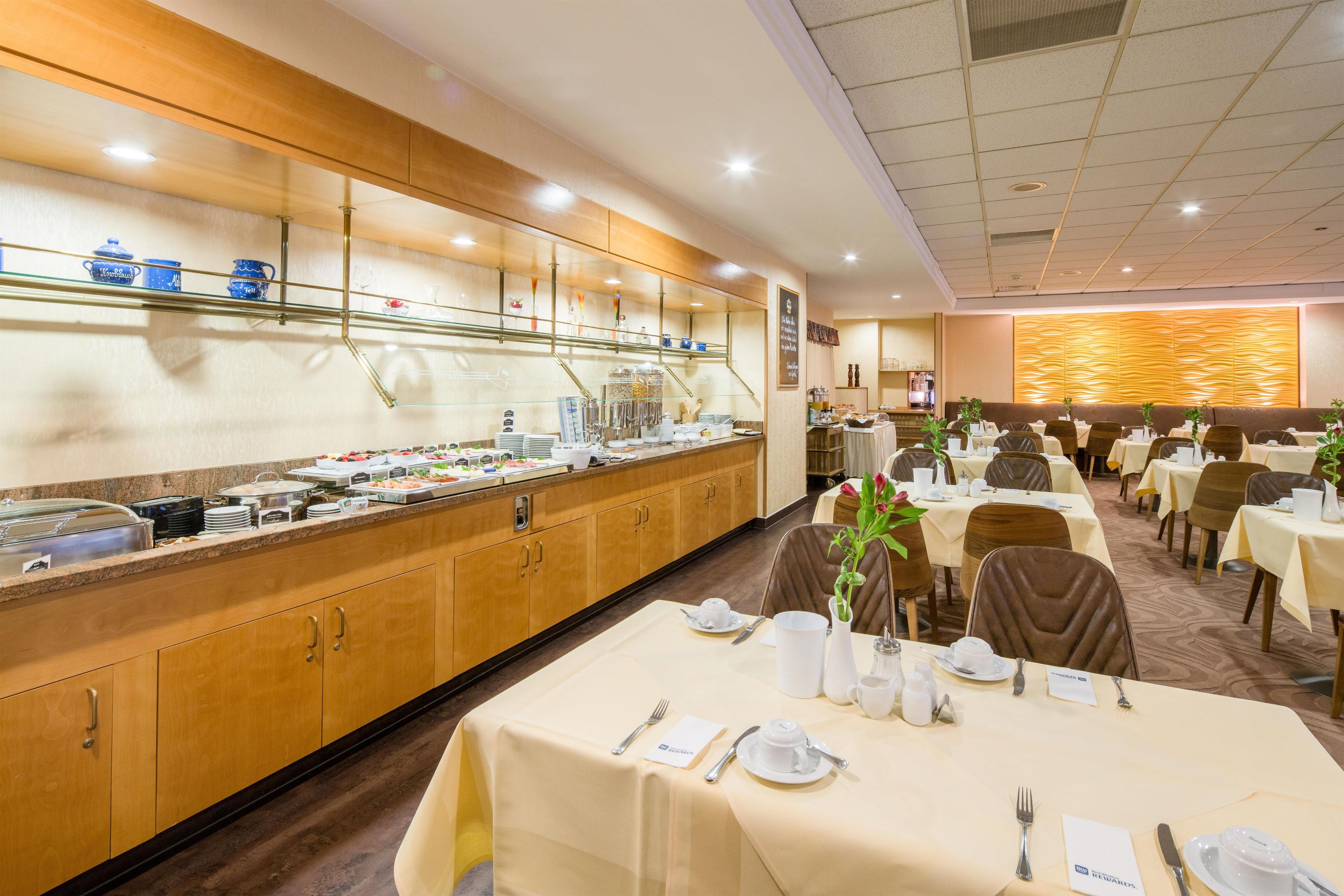 A buffet area with a variety of food options, a seating area with tables set for dining, and a decorative wall with a wavy pattern.