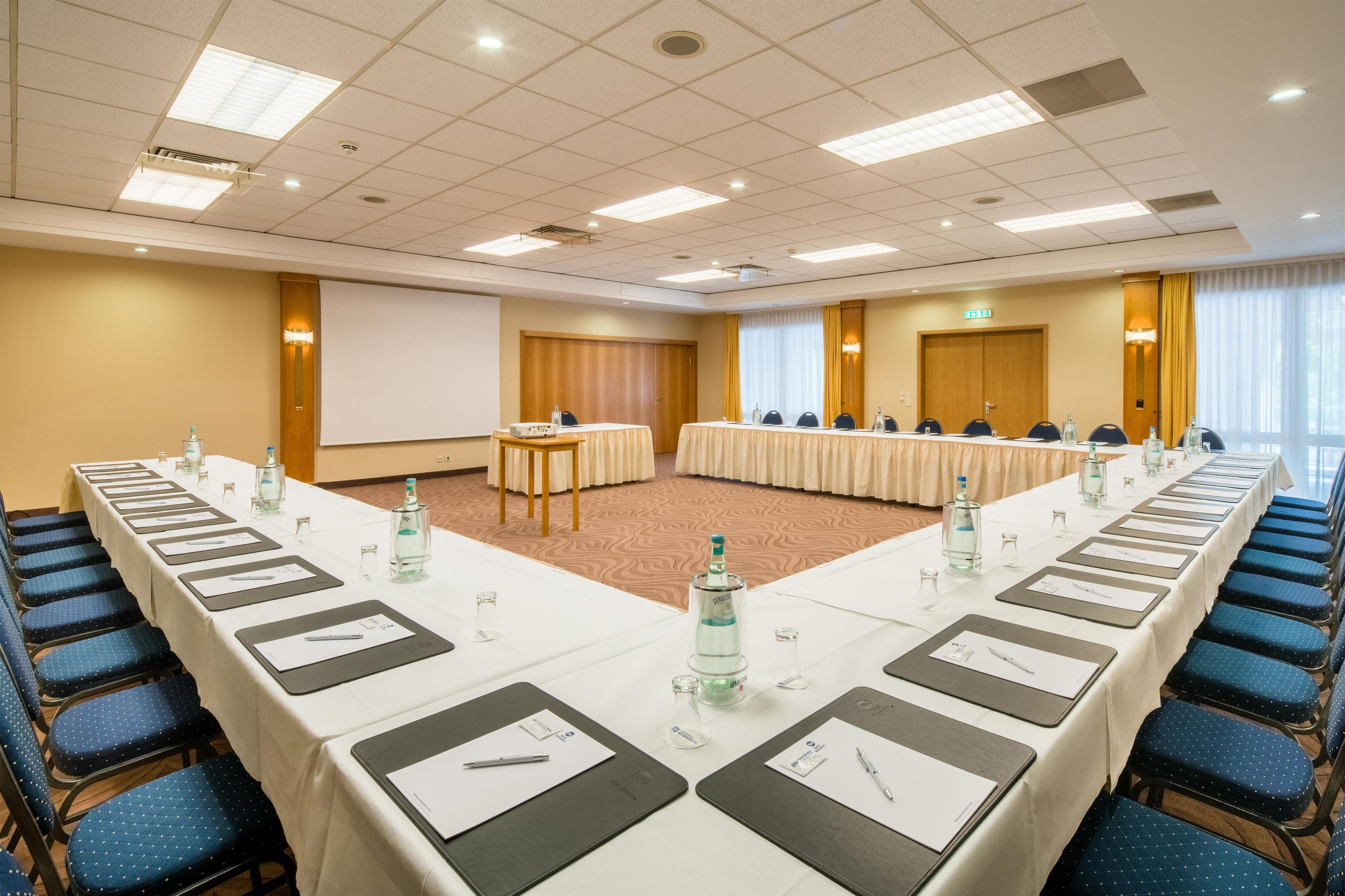 Ein Konferenzraum mit einem langen Tisch, Stühlen und einer Projektionsleinwand.