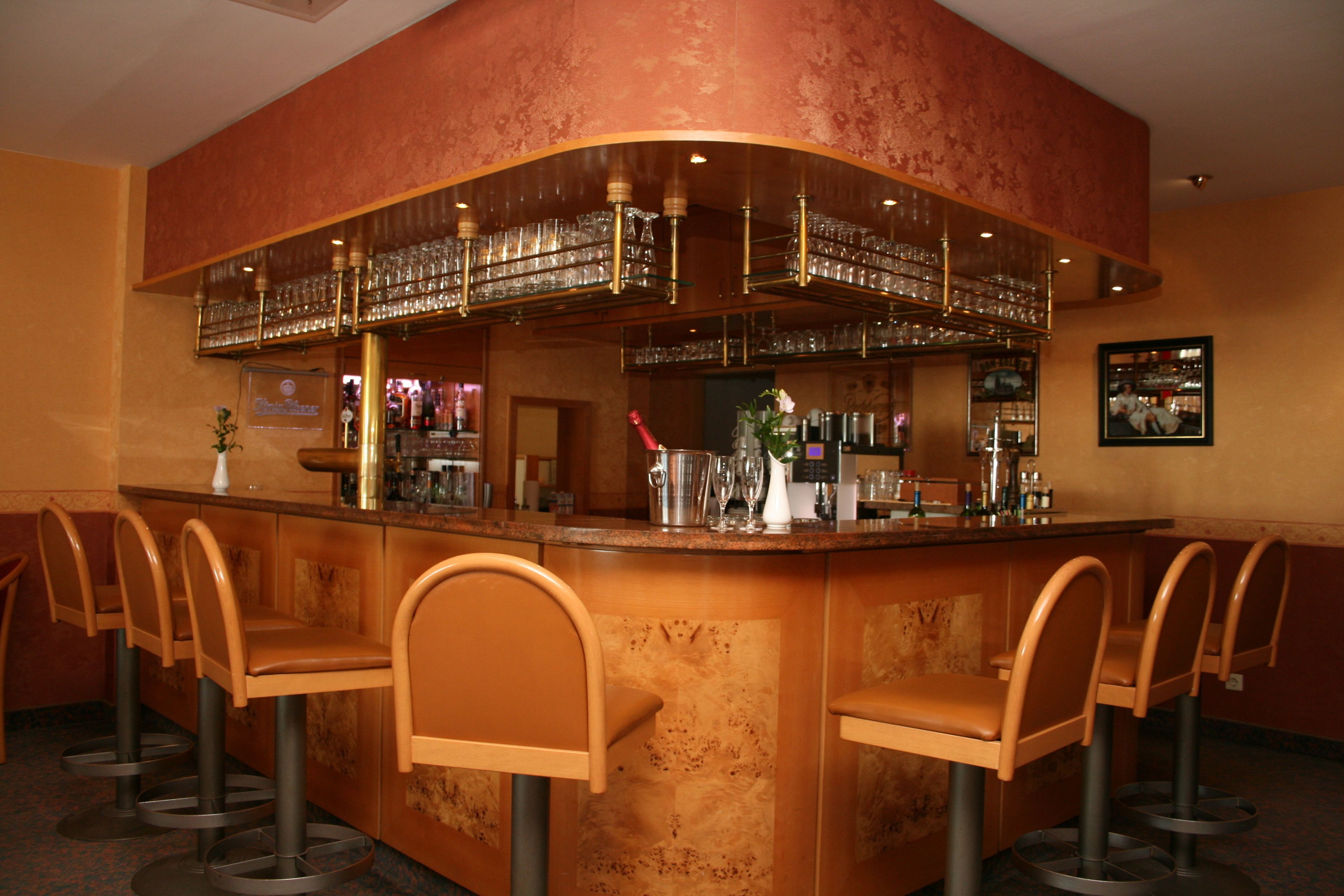 Un espace bar doté d’un comptoir incurvé, de nombreux tabourets et d’une variété de verres et de bouteilles.