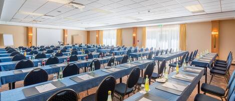 Une salle de conférence avec des rangées de tables, de chaises et des bouteilles d’eau.