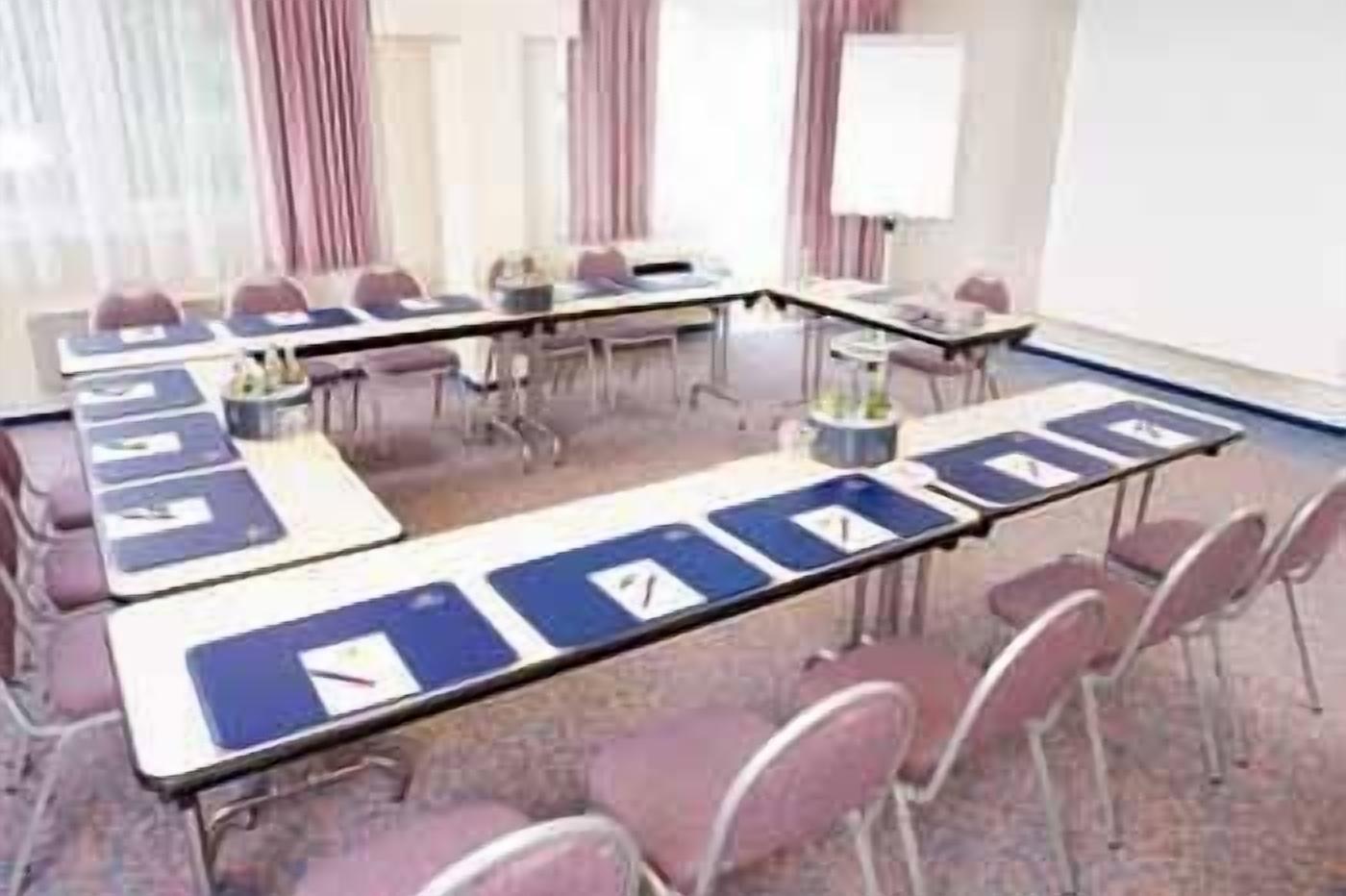 Een vergaderzaal met lange tafels, stoelen en een whiteboard.