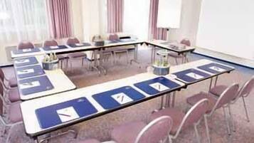 Een vergaderzaal met lange tafels, stoelen en een whiteboard.