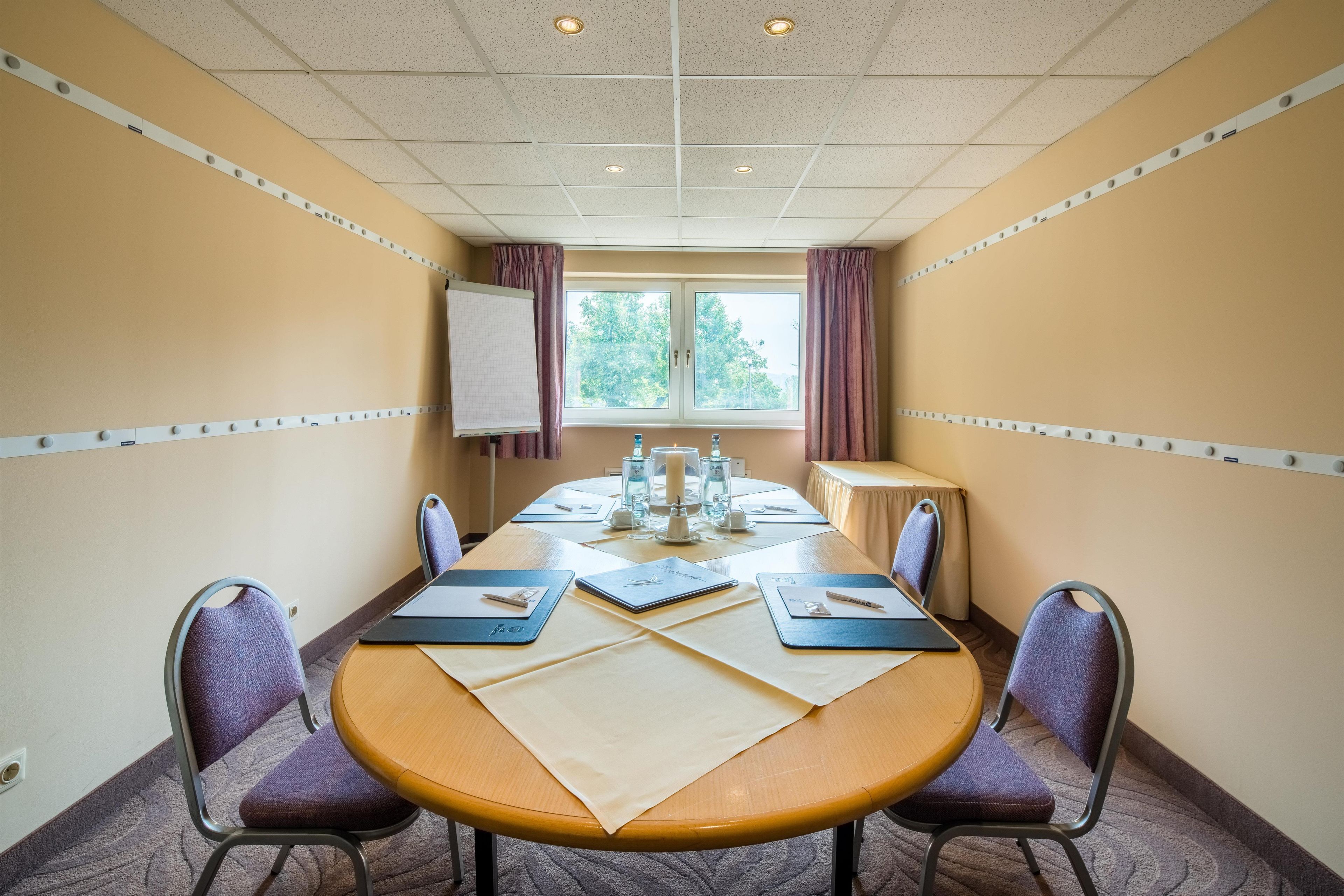 Een vergaderruimte met een lange tafel, stoelen, een whiteboard en een raam met gordijnen.