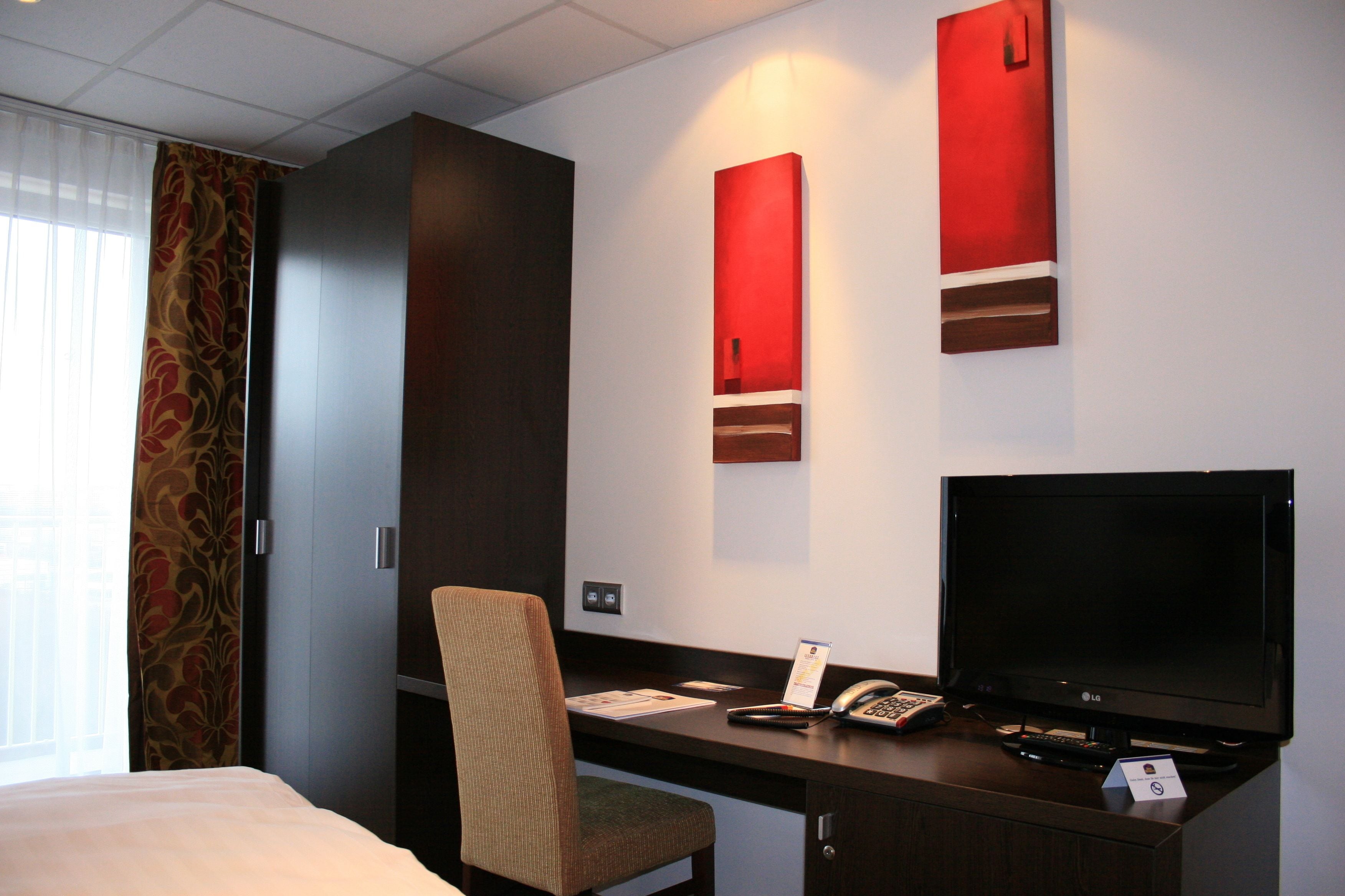 A hotel room with a bed, a desk with a chair, a television, and a telephone.