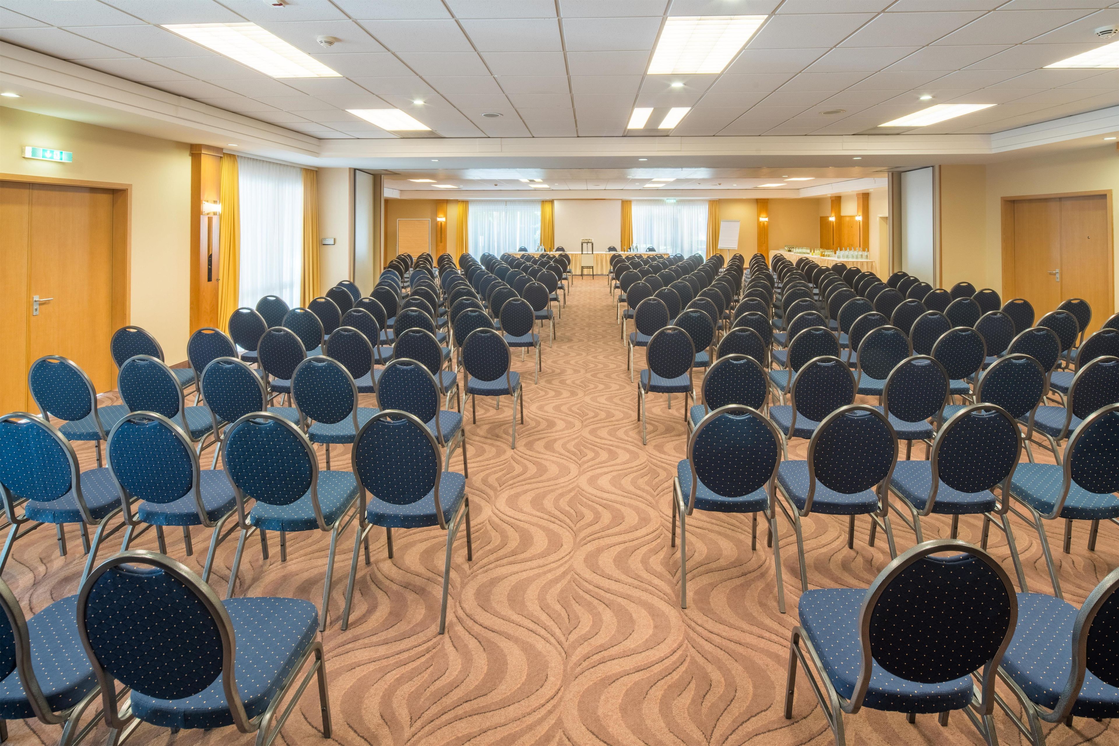 A conference room with rows of chairs, a stage, and a carpeted floor.