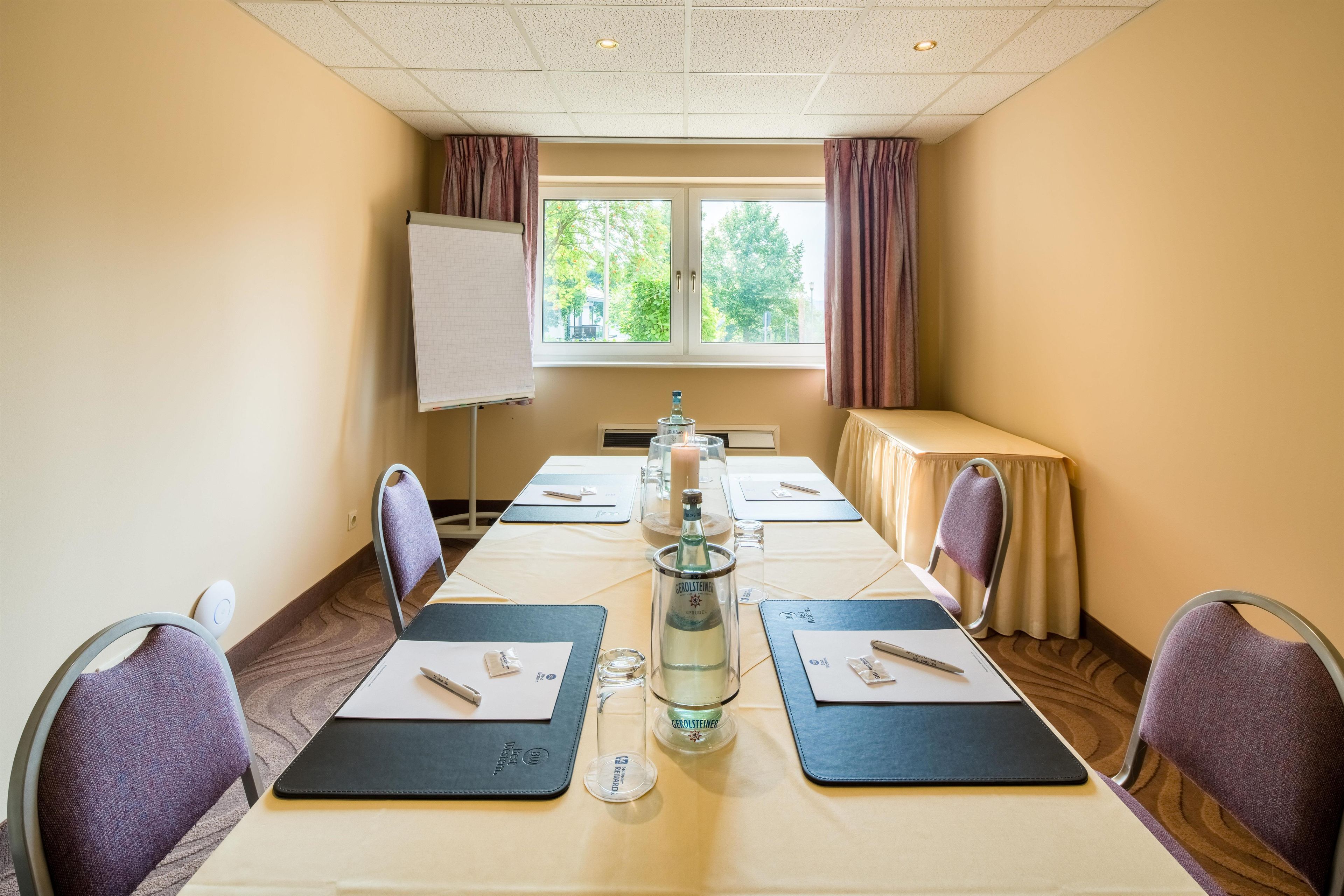 A conference room with a long table, chairs, a projector screen, and a window with curtains.