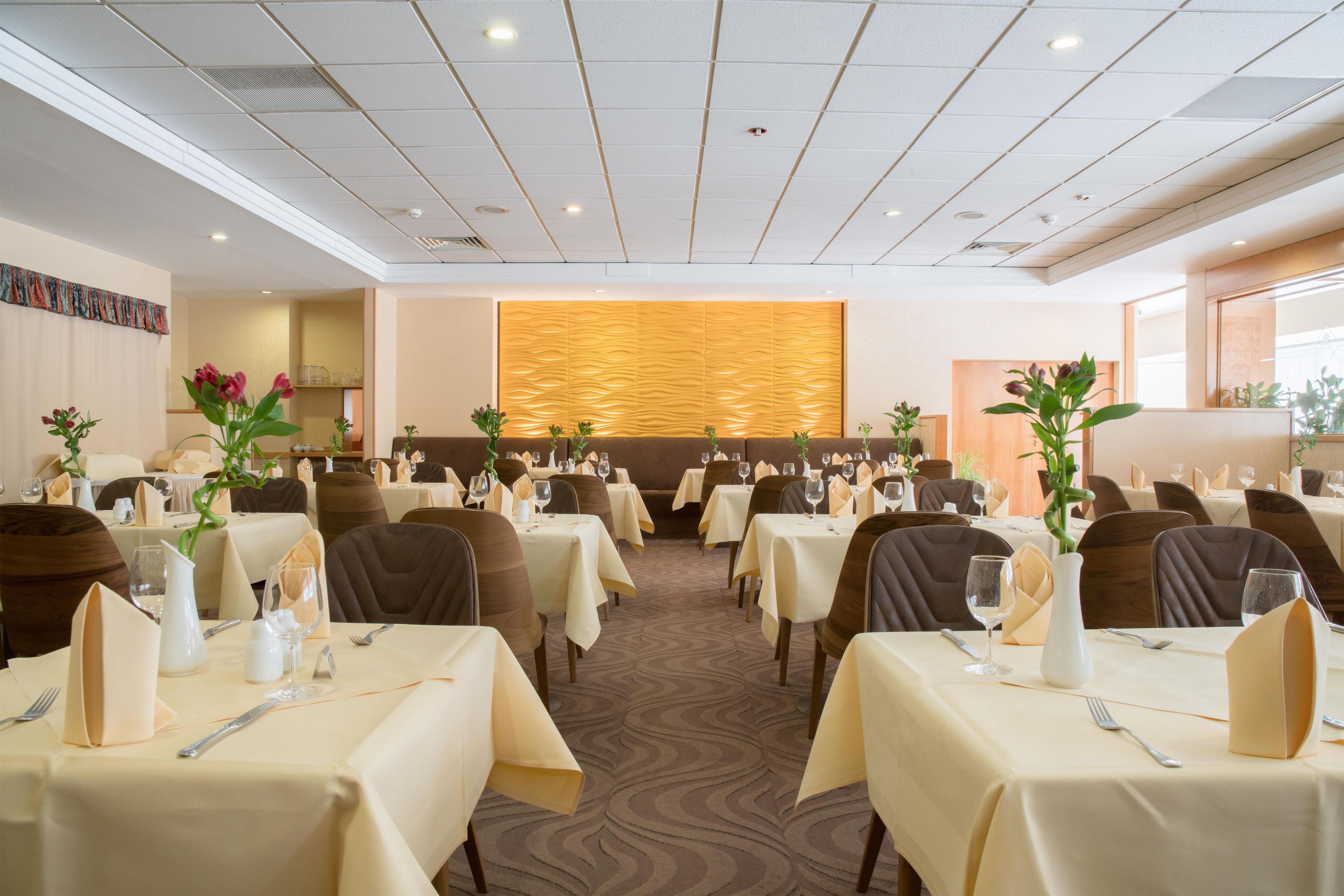 En hotellrestaurang med flera bord som är dukade för gästerna, med ett mönstrat golv och en dekorativ vägg.