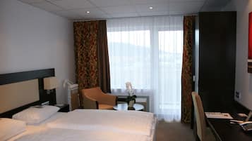 Ein Hotelzimmer mit zwei Betten, einem Schreibtisch, einem Stuhl, einem kleinen Tisch und einem Fenster mit Vorhängen.