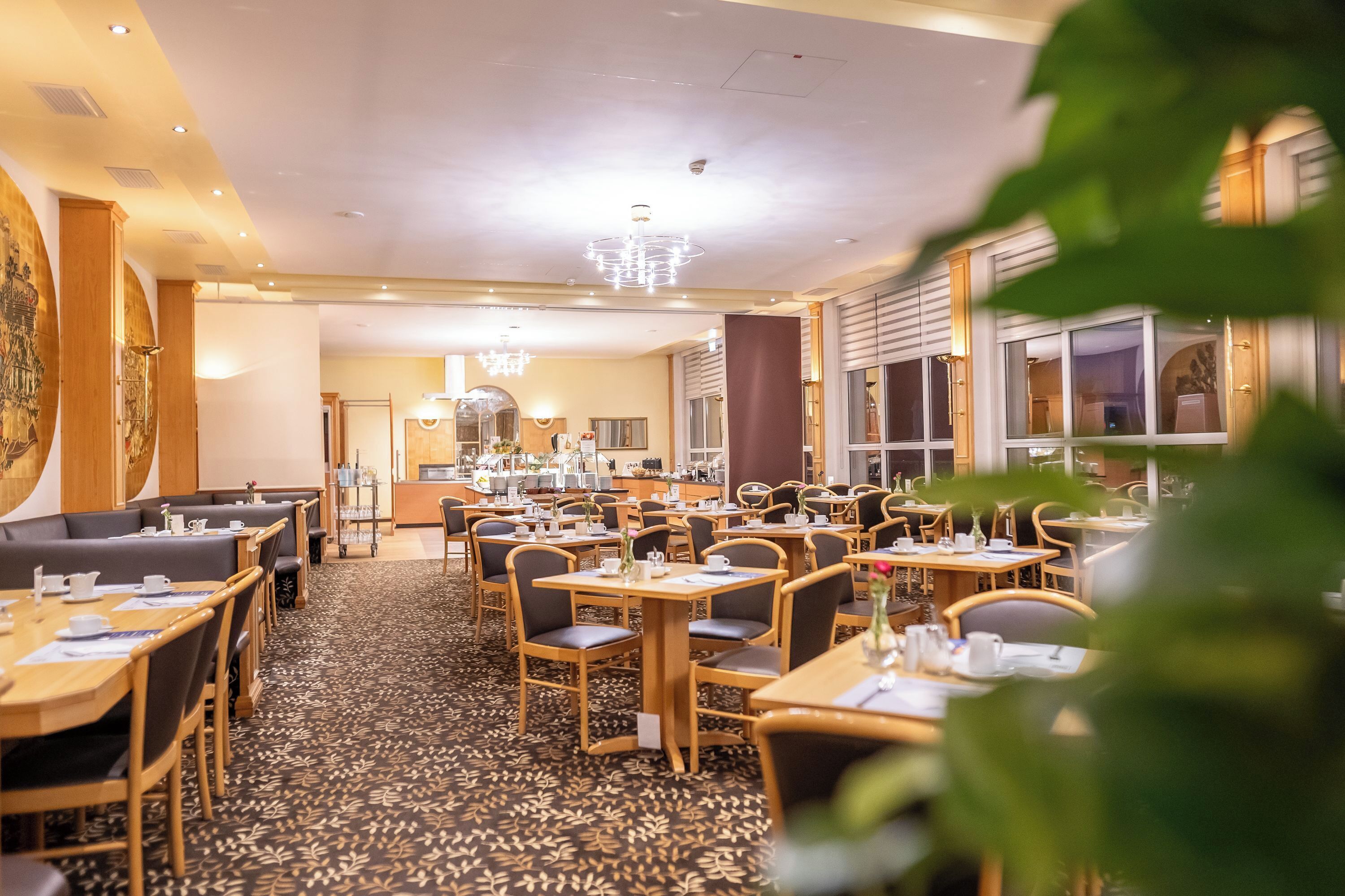 Ein Hotel-Essbereich mit mehreren Tischen und Sitzgelegenheiten, einem gemusterten Teppich und einer Kronleuchter.