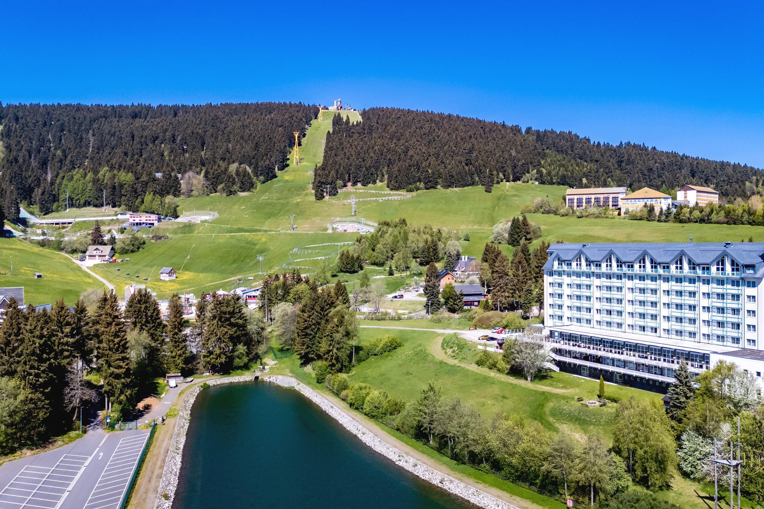 A hotel with a large building, a lake, and a forested hill in the background.