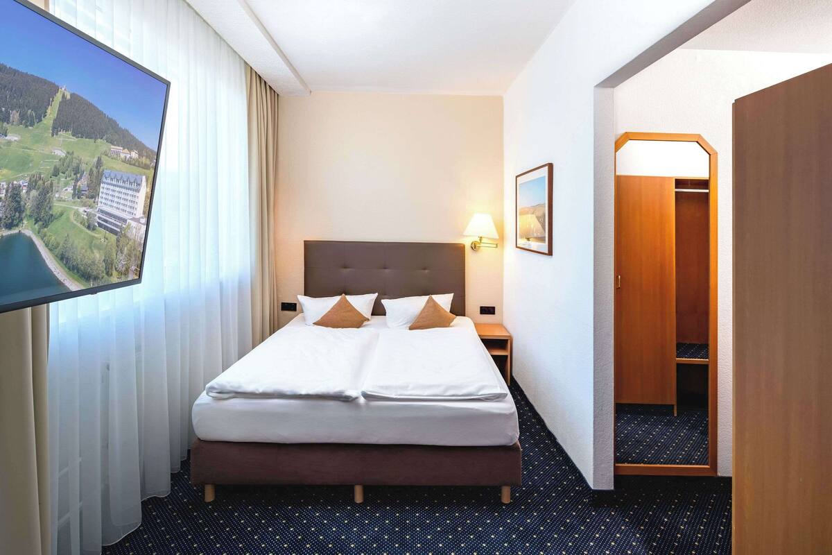 Une chambre d’hôtel avec un grand lit, un téléviseur fixé au mur, une table de chevet, une lampe et une armoire en bois.