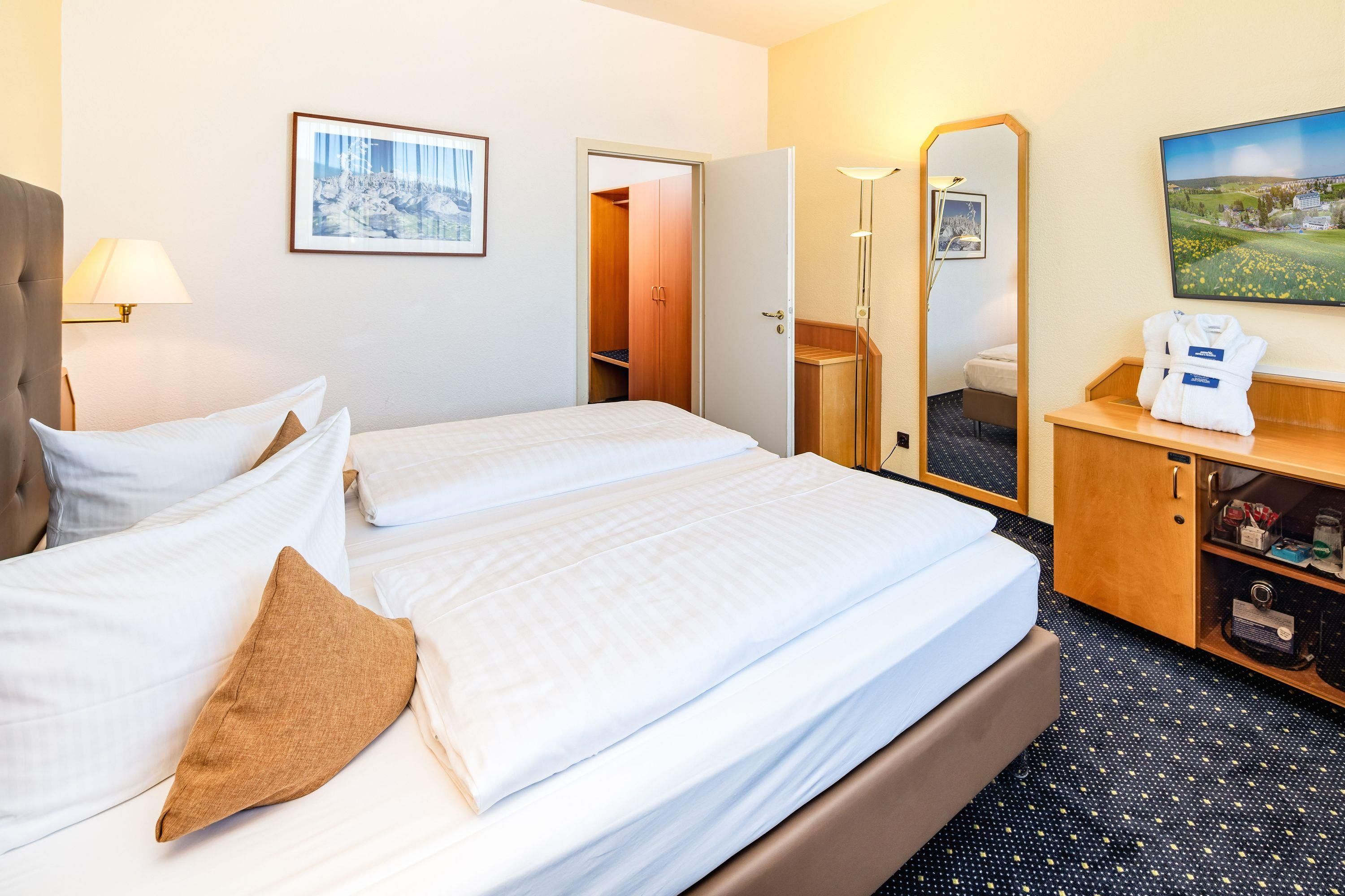 Ein Hotelzimmer mit einem großen Bett, einem Nachttisch mit Lampe, einem Kleiderschrank und einem Spiegel.