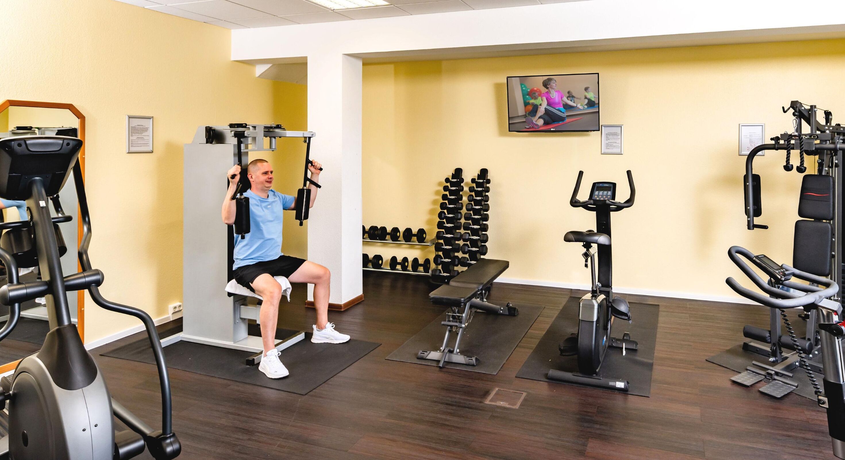 Un gimnasio con equipo de ejercicio, una televisión y una pared con mancuernas.
