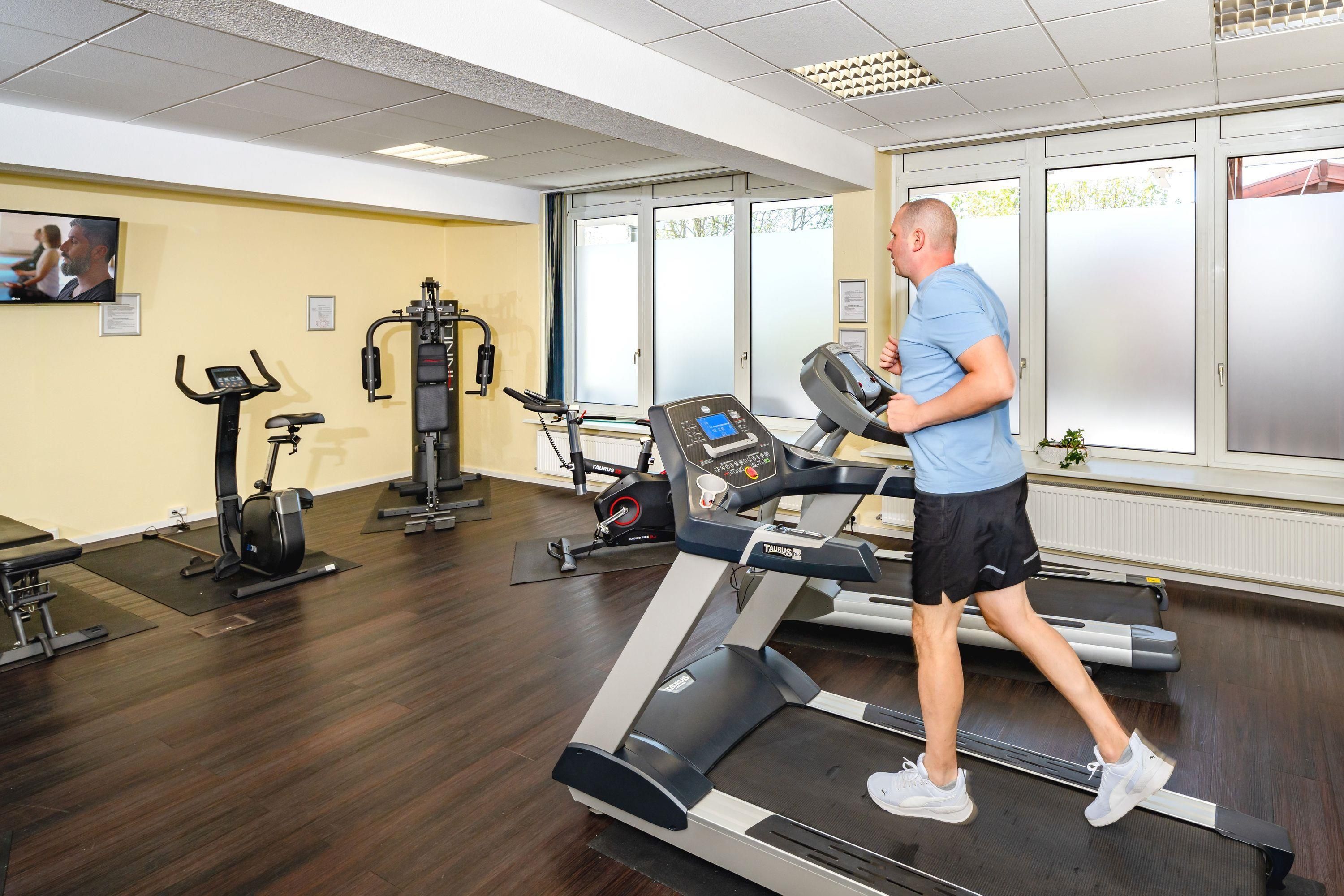A gym with a treadmill, exercise bikes, and a mirrored wall.