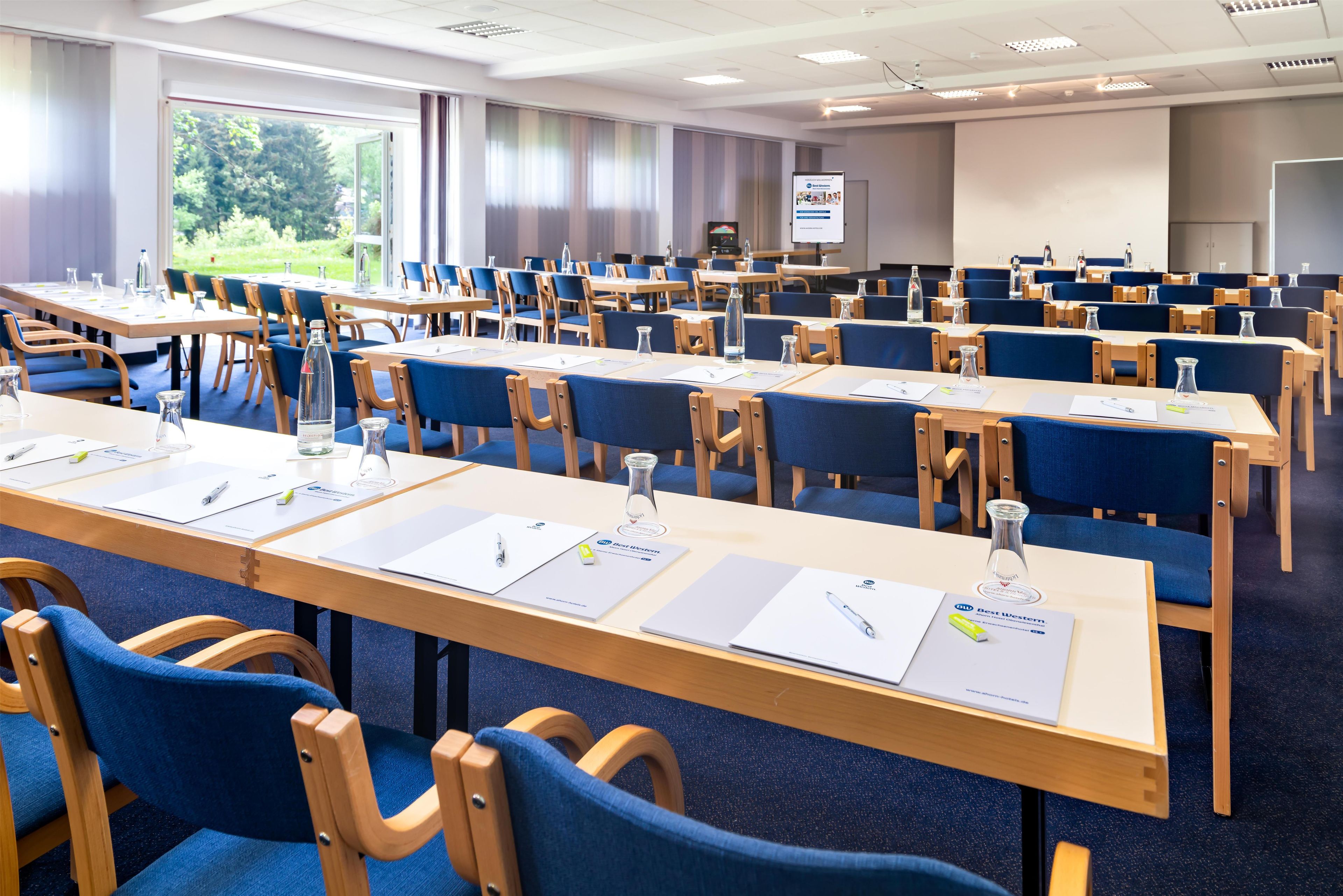 Un salón de conferencias con filas de mesas y sillas, equipado con botellas de agua y tarjetas de identificación.