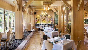 A restaurant with wooden paneling, large windows, and a chandelier. Tables are set with white tablecloths and candles. - Best Western Ahorn Hotel Oberwiesenthal - Adults Only (Oberwiesenthal)