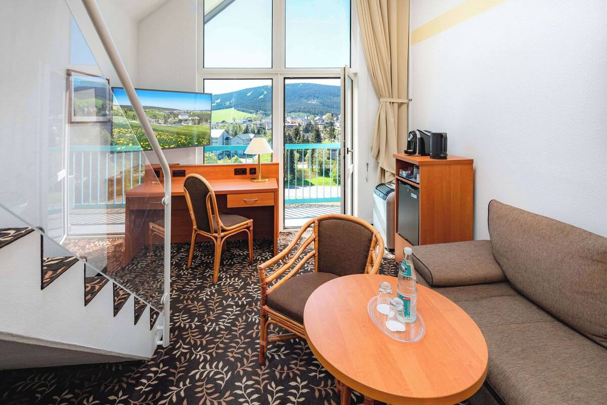 Une chambre d’hôtel avec un balcon, un bureau, une chaise, un canapé, une petite table et une machine à café.