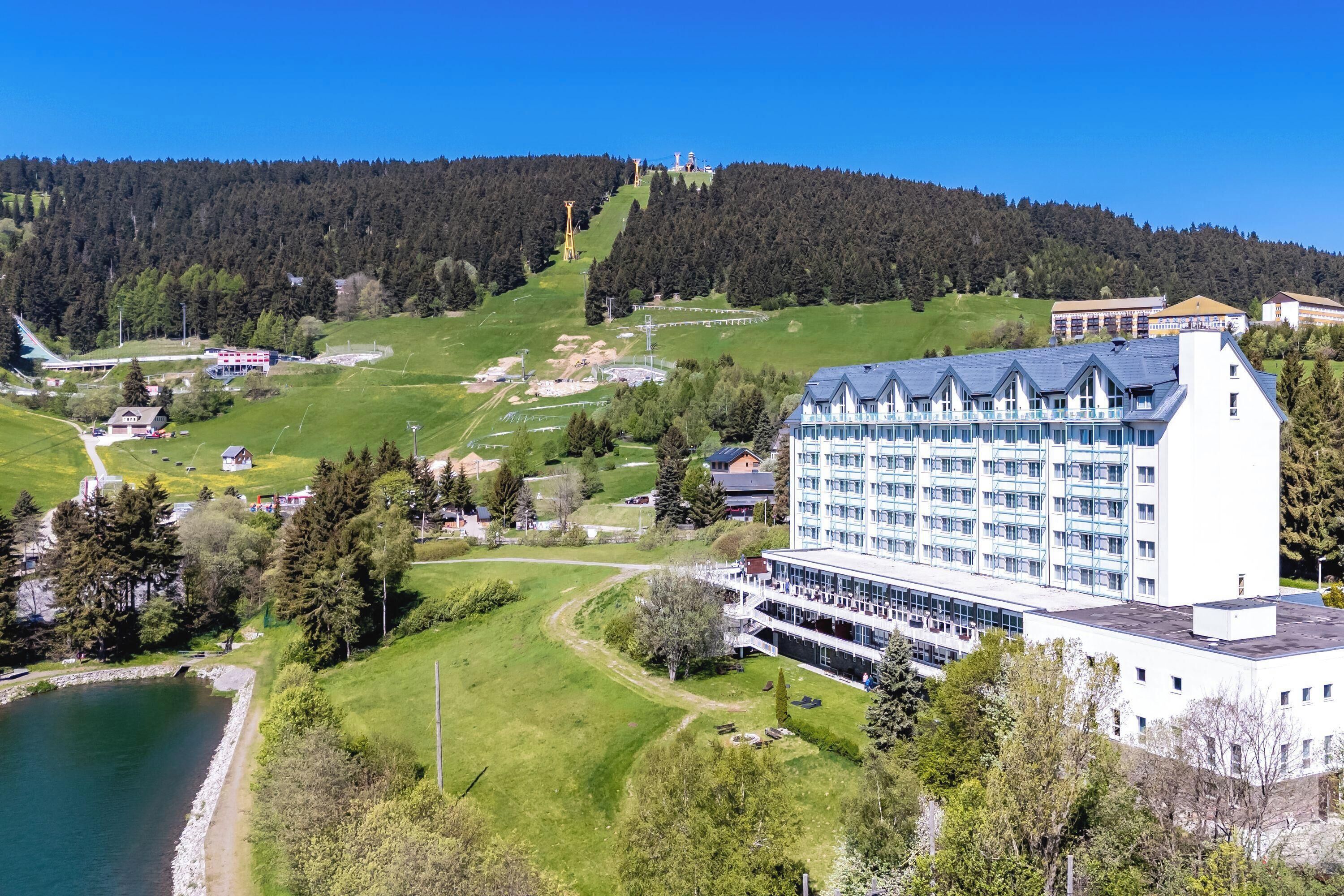 Un hotel grande con varios pisos, piscina y vista a una colina boscosa.