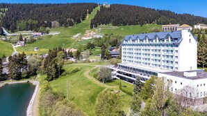 A large hotel with multiple floors, a swimming pool, and a view of a forested hill.