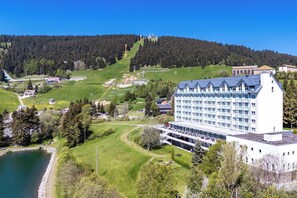 A large hotel with multiple floors, a swimming pool, and a view of a forested hill.