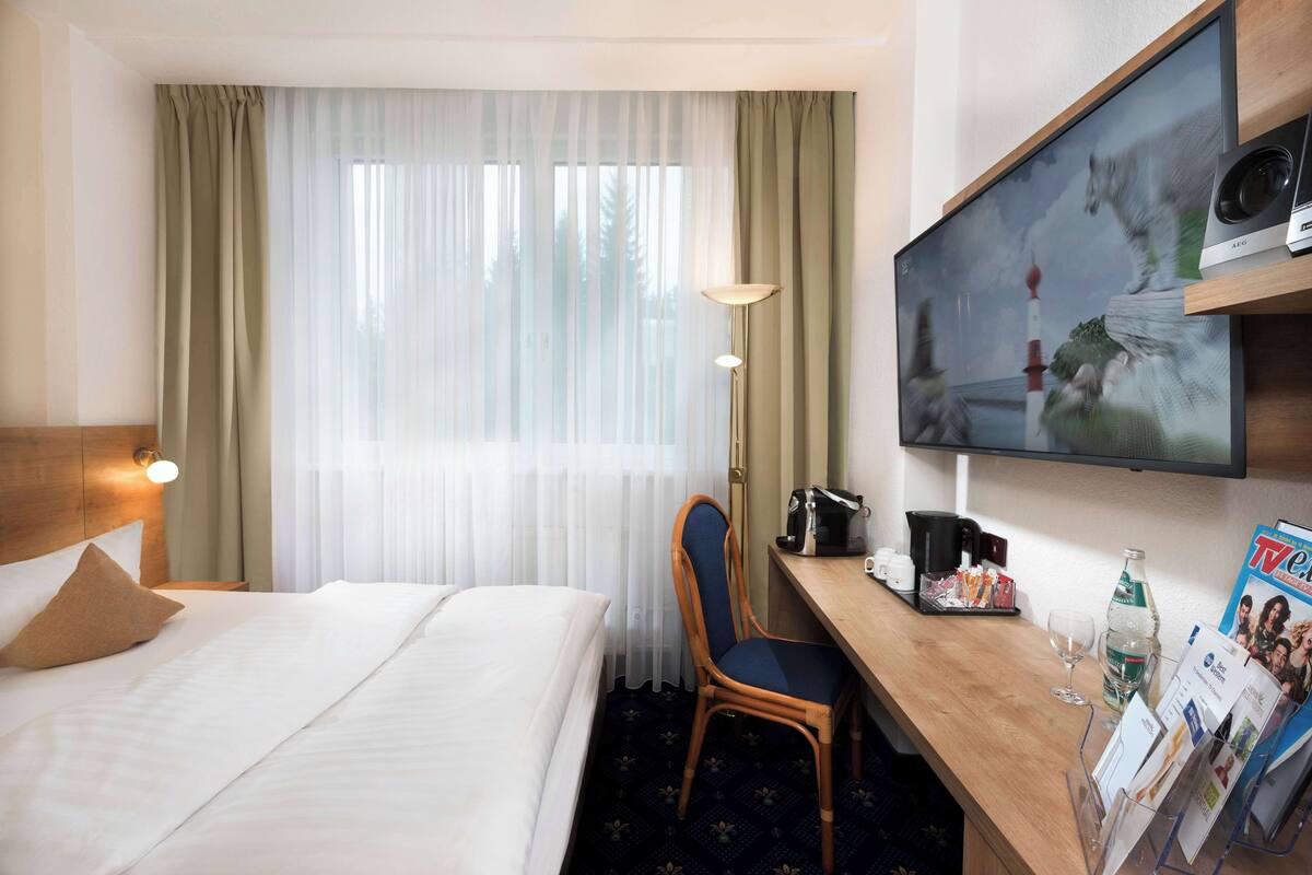 Une chambre d’hôtel comprenant un lit, un bureau avec une chaise, une télévision et un porte-revues.
