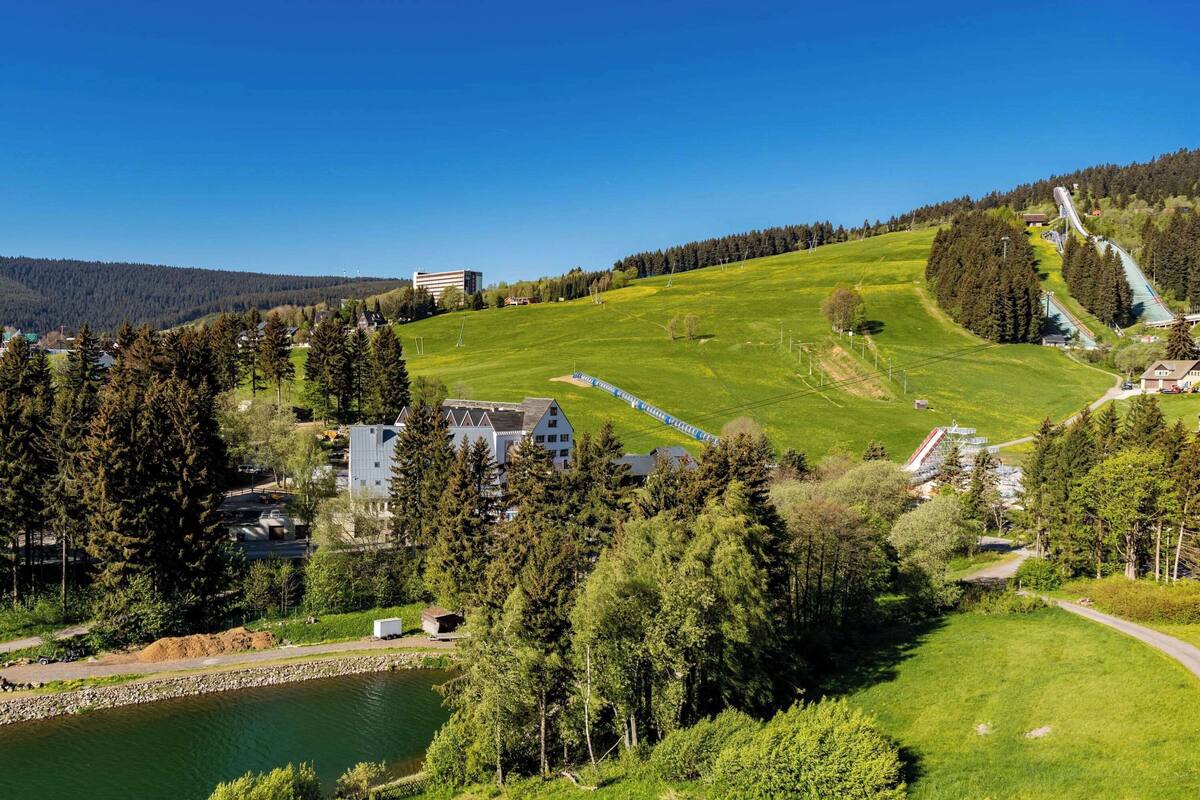 Une vue pittoresque d’une vallée verdoyante, avec un lac, une piste de ski et des immeubles résidentiels.