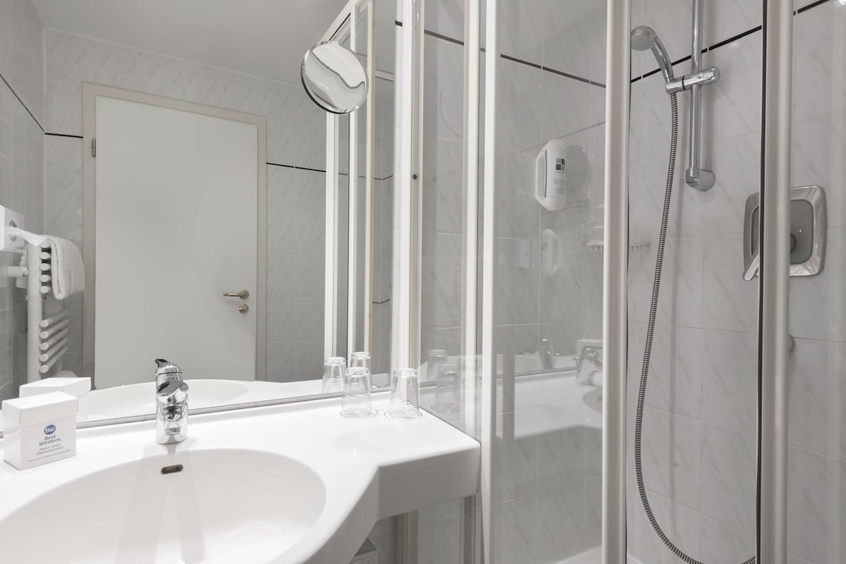 A modern bathroom with a white sink, a glass shower enclosure, and a large mirror.