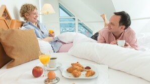 A couple in a bedroom with a breakfast setup including croissants, an apple, orange juice, and coffee.