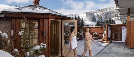 Un bâtiment en bois avec une porte en verre, entouré d’arbres couverts de neige et sous un ciel dégagé.