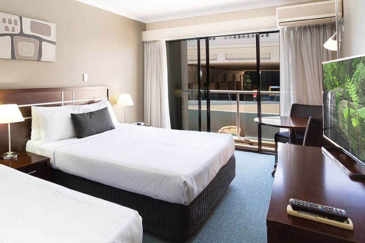Une chambre d’hôtel avec deux lits, un bureau avec une télévision et un balcon donnant sur l’extérieur.
