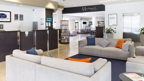 A hotel lobby with a reception desk, two sofas, a coffee table, and a dining area in the background. - Riverside Hotel Southbank (South Brisbane)