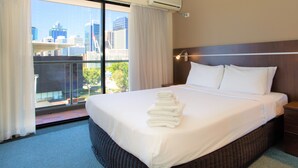 A hotel room with a large bed, a nightstand, a wall-mounted lamp, and a view of a cityscape through a large window. - Riverside Hotel Southbank (South Brisbane)