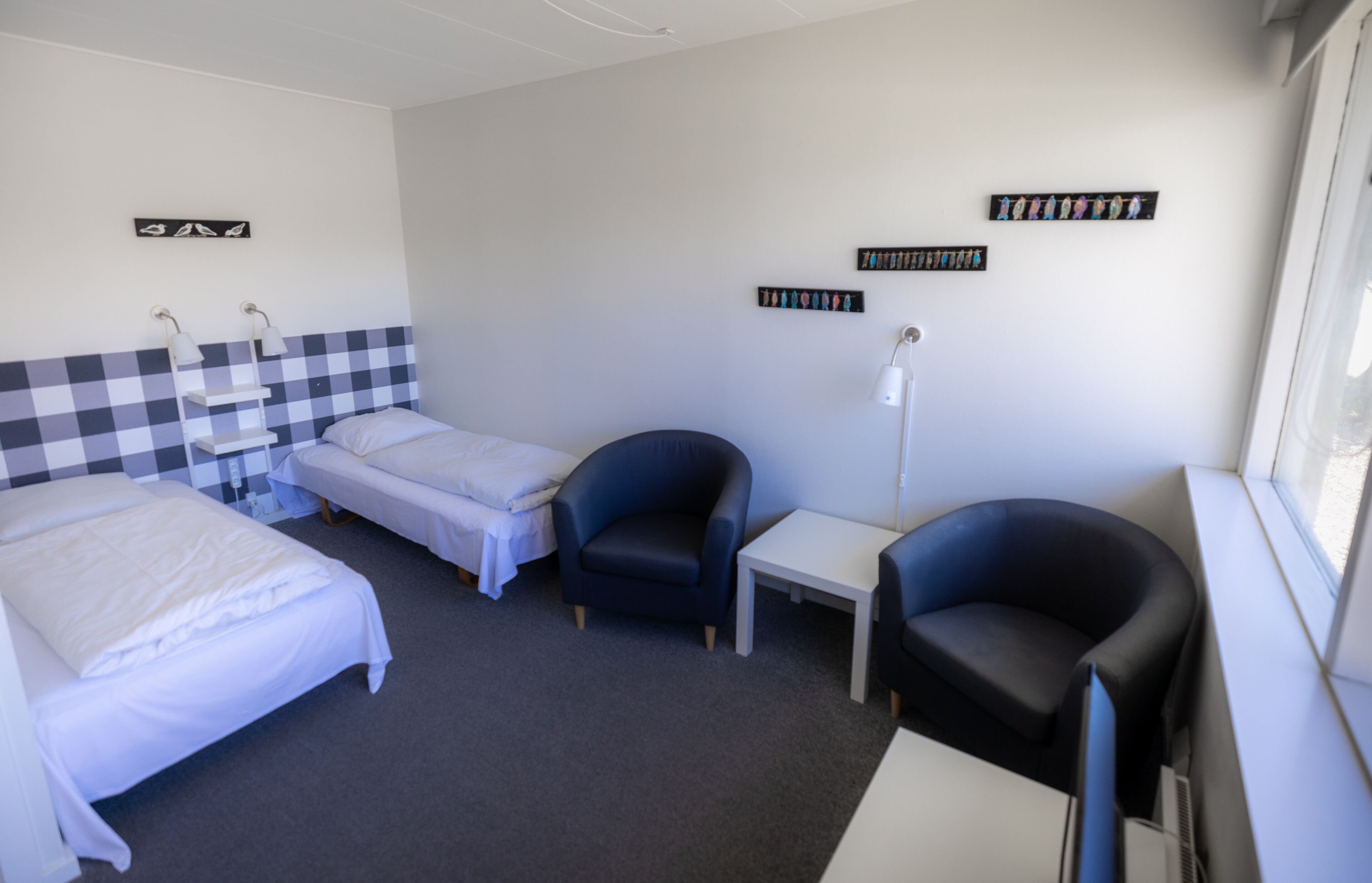 A hotel room with two single beds, a desk, two chairs, and a window.