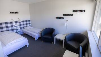 A hotel room with two single beds, a desk, two chairs, and a window.