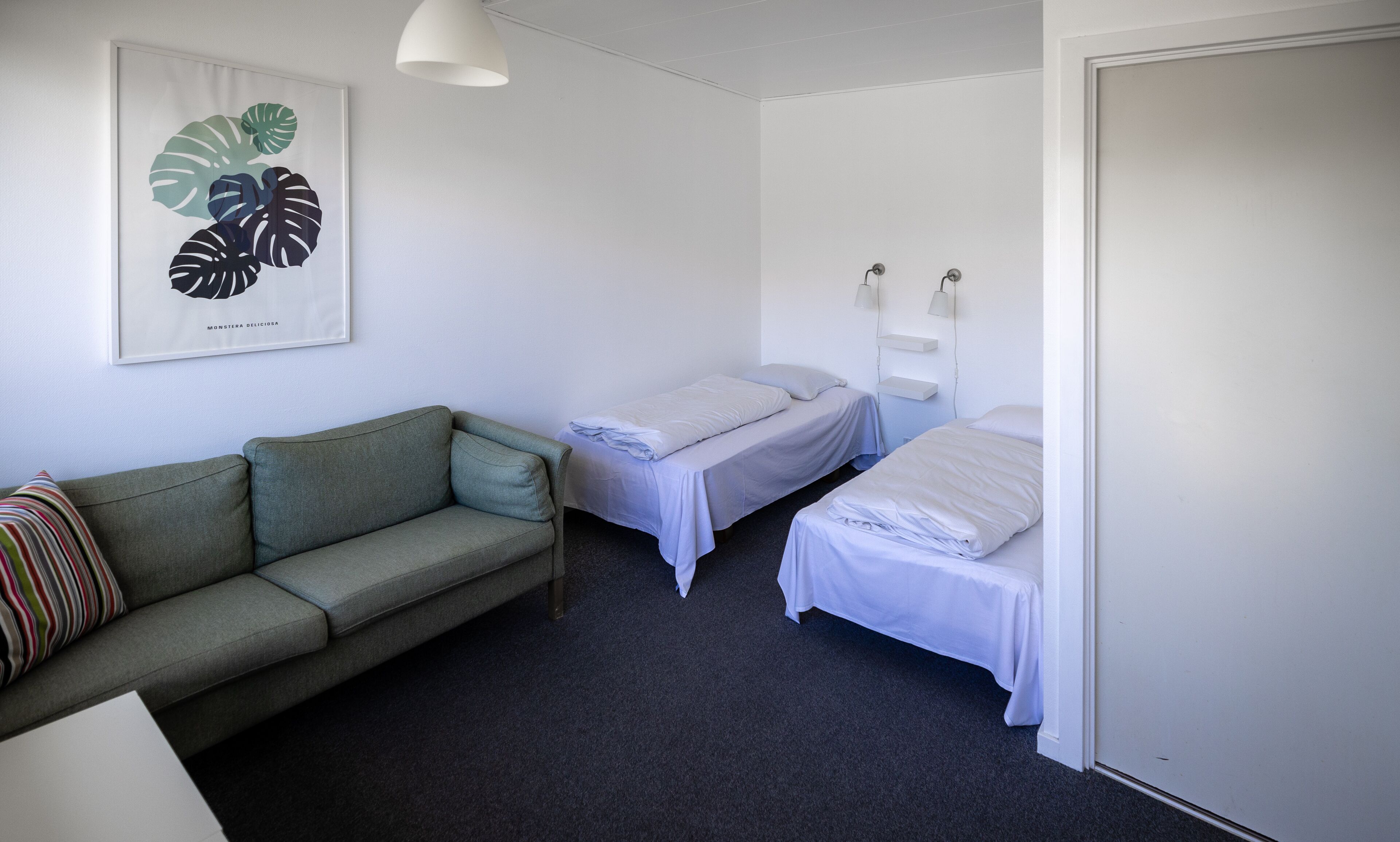 Una habitación pequeña y limpia con un sofá verde, dos camas individuales, una obra de arte enmarcada y una puerta blanca.