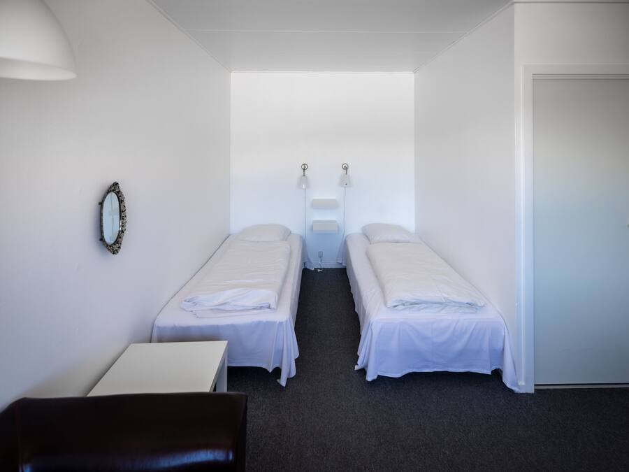A small, clean room with two single beds, a desk, a chair, and a mirror on the wall.