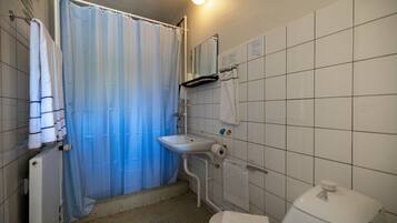 A bathroom with a shower, sink, toilet, and tiled walls.