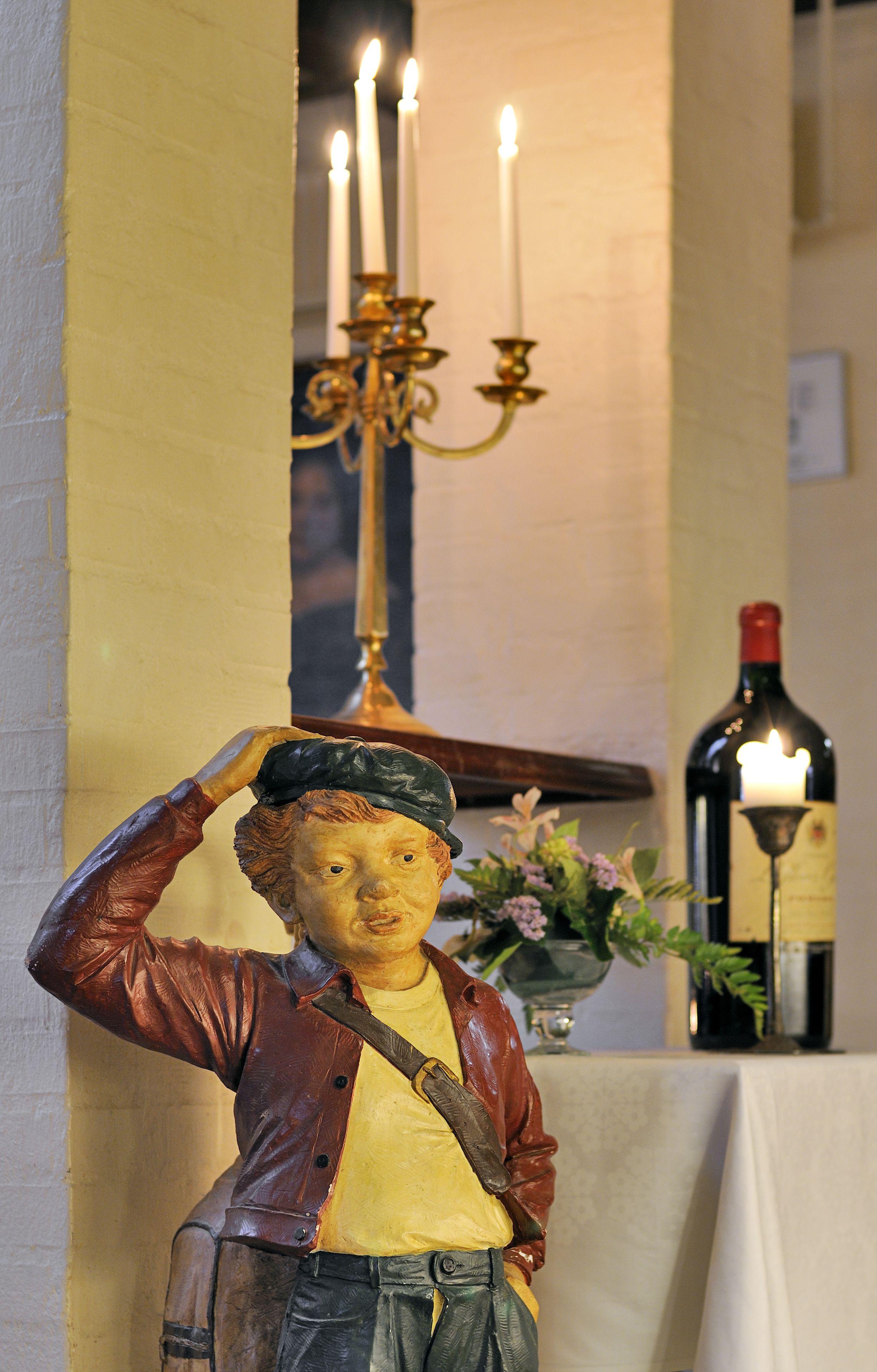 A statue of a man saluting, a candle, and a bottle of wine on a table.