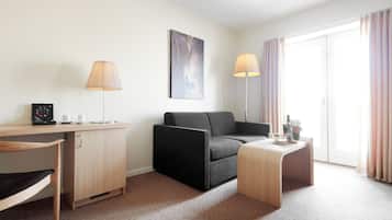Una habitación de hotel moderna con un escritorio de madera, un sofá negro, una pequeña mesa de madera y un ventanal con cortinas.