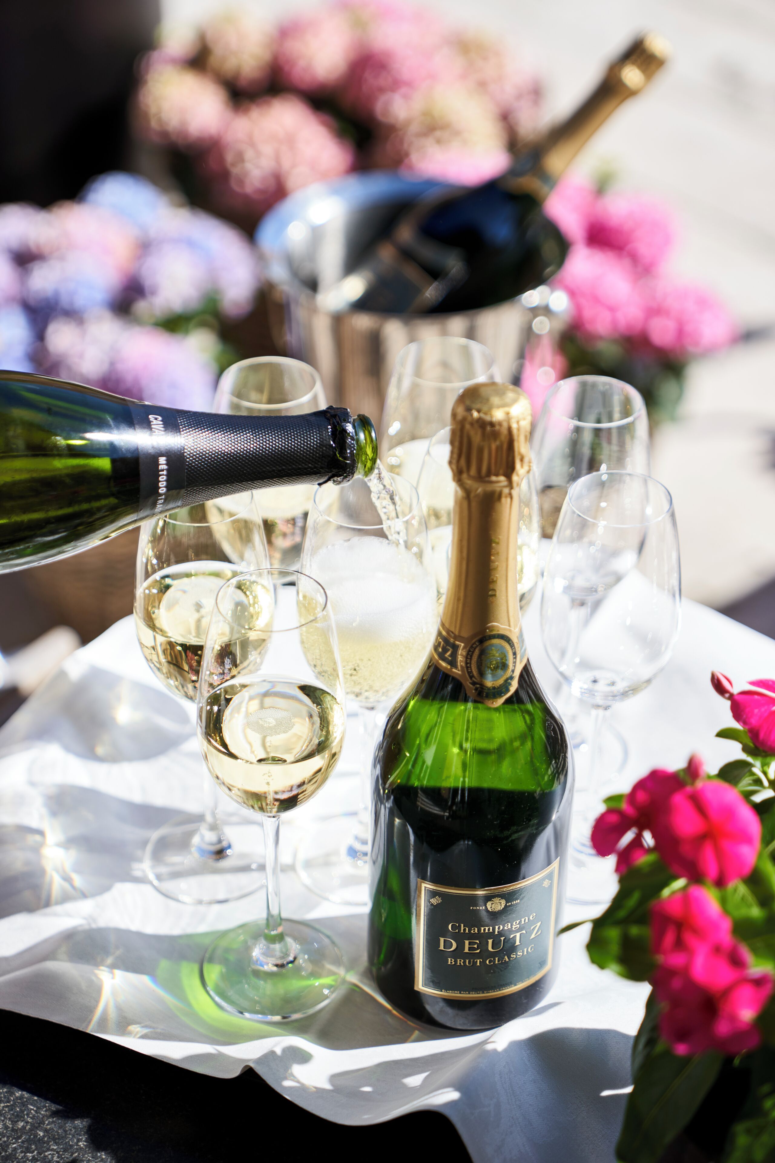 A table with a bottle of champagne and glasses, surrounded by flowers.