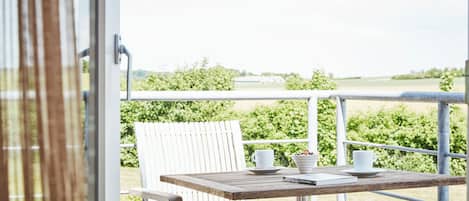 A balcony with a table and chairs, a white chair, and a view of a green field.