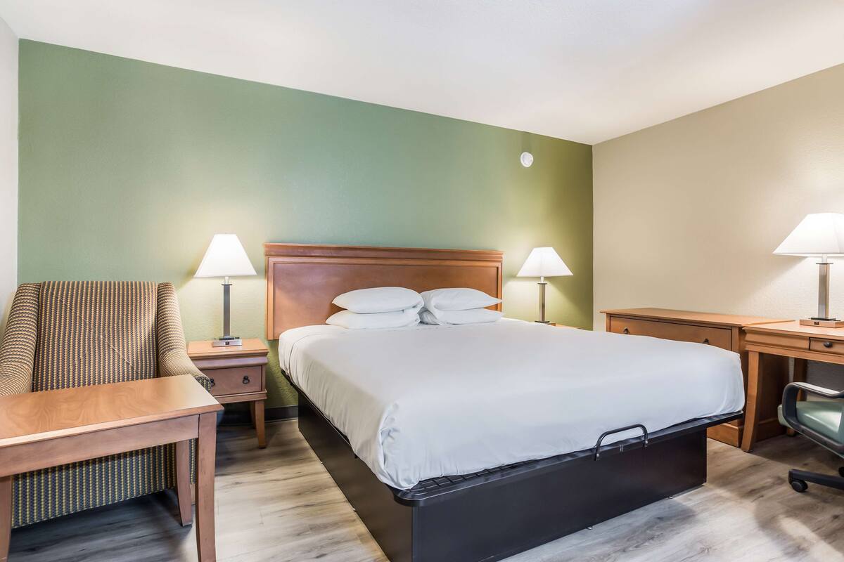 A hotel room with a bed, a chair, a desk, and two lamps.