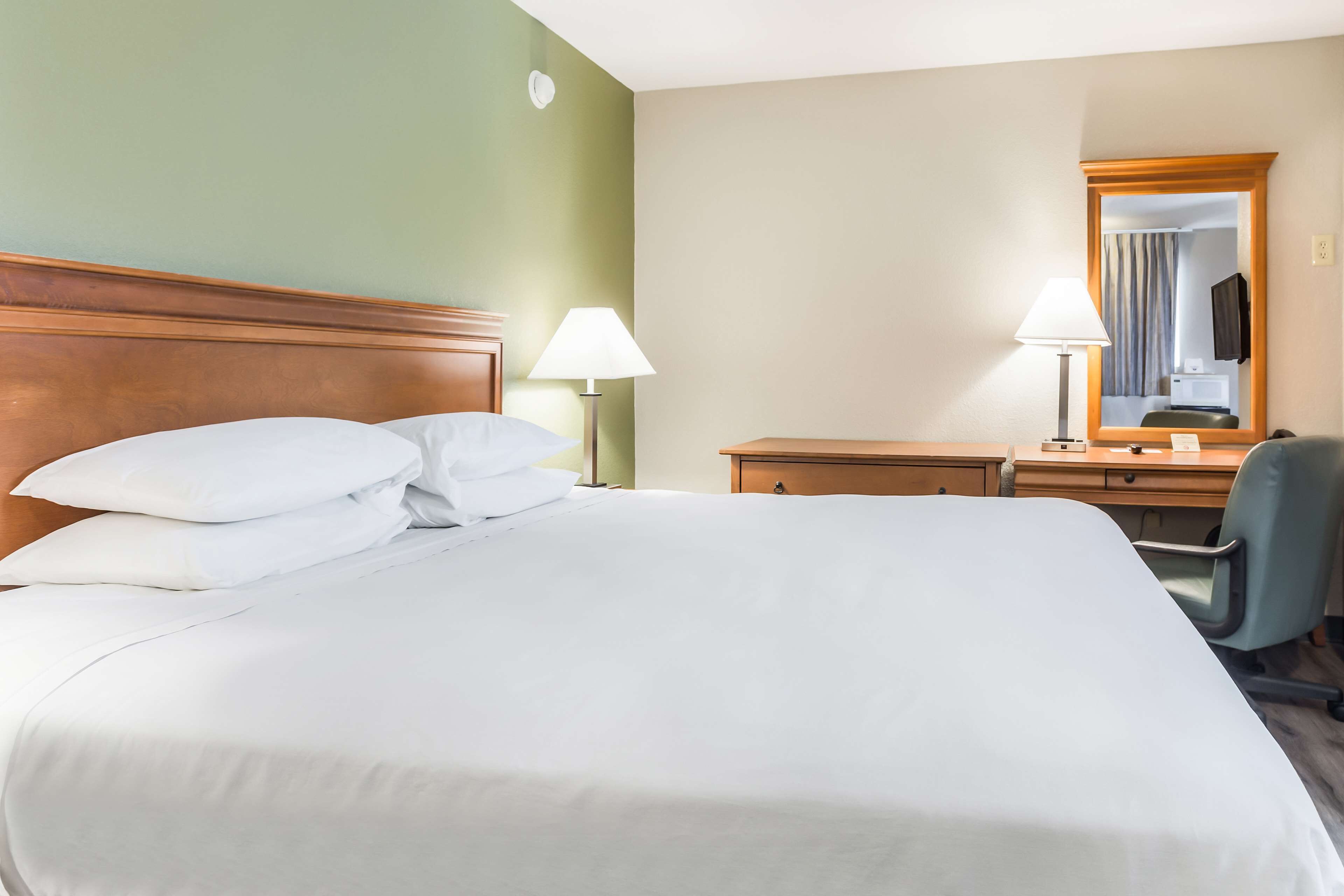 Una habitación de hotel con una cama grande, un escritorio, una silla y un espejo.