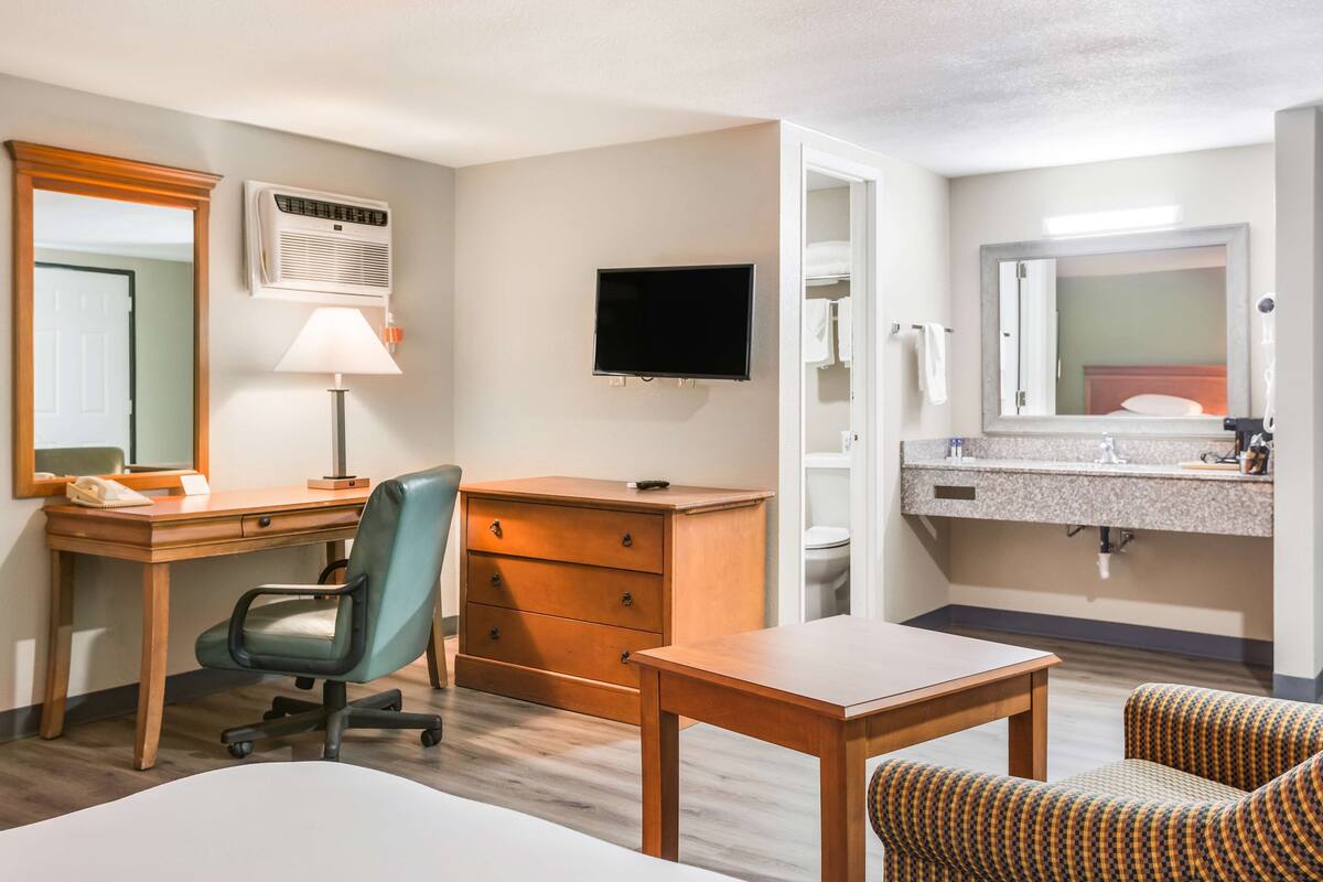 A hotel room with a desk, chair, bed, TV, and bathroom.